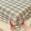 A close-up of a plaid fitted sheet in gray and beige tones being held by hands.
