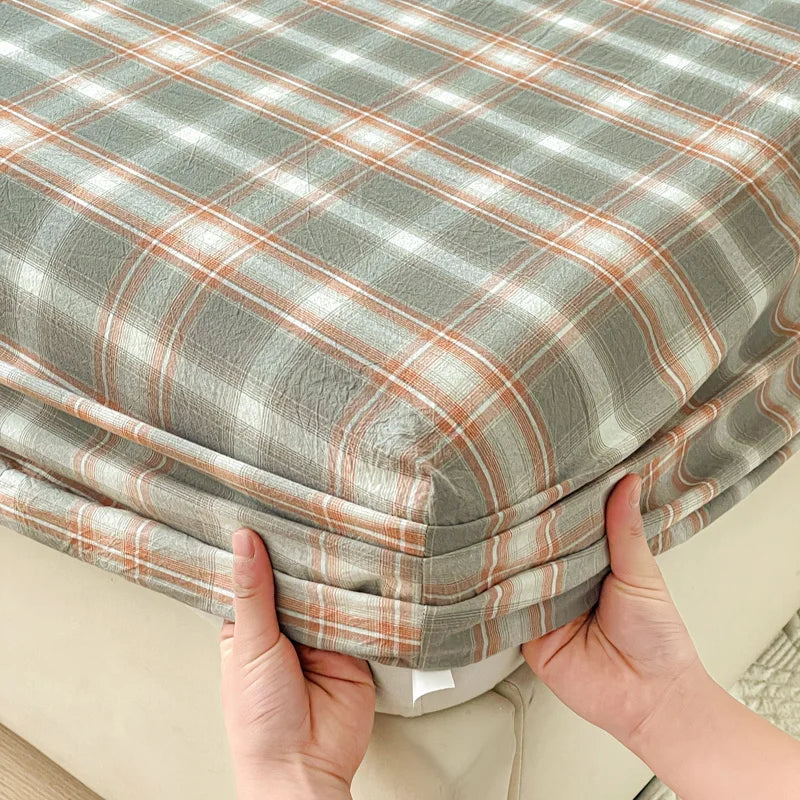 A close-up of a plaid fitted sheet in gray and beige tones being held by hands.