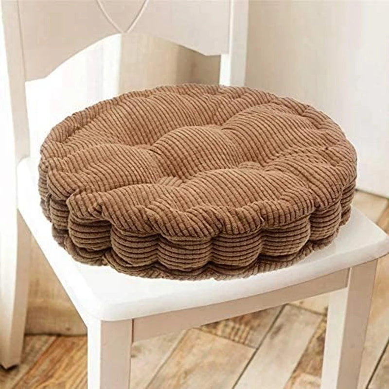 A round, tufted corduroy floor seat cushion in a brown color resting on a white wooden chair.