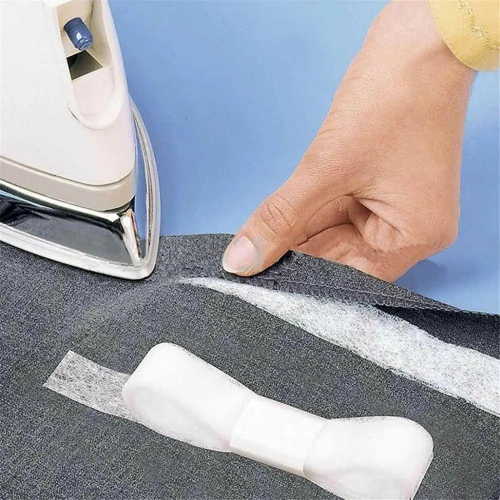 A hand is applying double-sided fabric interlining tape to a dark gray fabric piece.