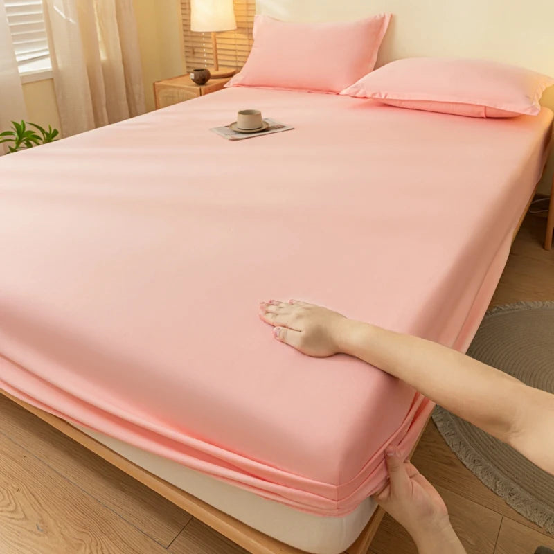 A pink fitted bed sheet is draped over a bed, with a hand visible touching the fabric.