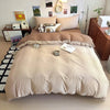 A beige quilt bedding set with decorative pillows and a white wooden headboard in a bright room.