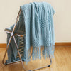 A light blue oversized knitted tassel throw blanket draped over a metal stand.