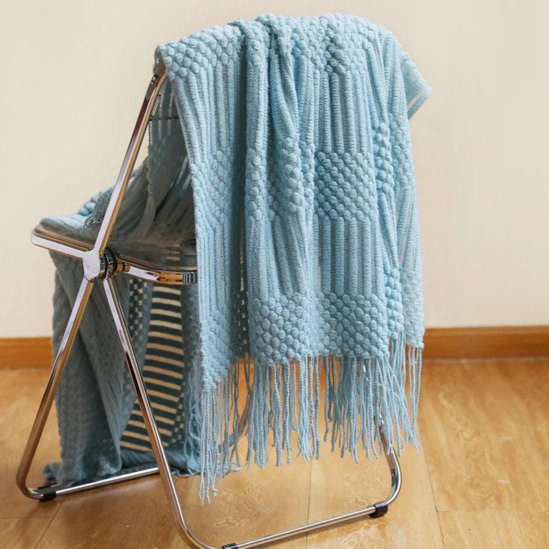 A light blue oversized knitted tassel throw blanket draped over a metal stand.