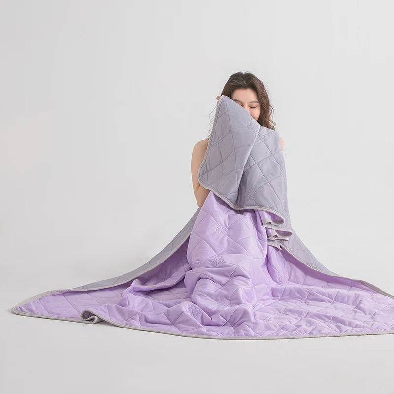 A purple lightweight cooling blanket is draped over a person's head and spread out on a light gray background.