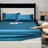 A teal fitted sheet and pillow set on a bed with a dark headboard and modern bedside lamp.
