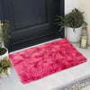 A vibrant pink faux fur area rug placed on a light gray floor next to a dark cabinet and potted greenery.