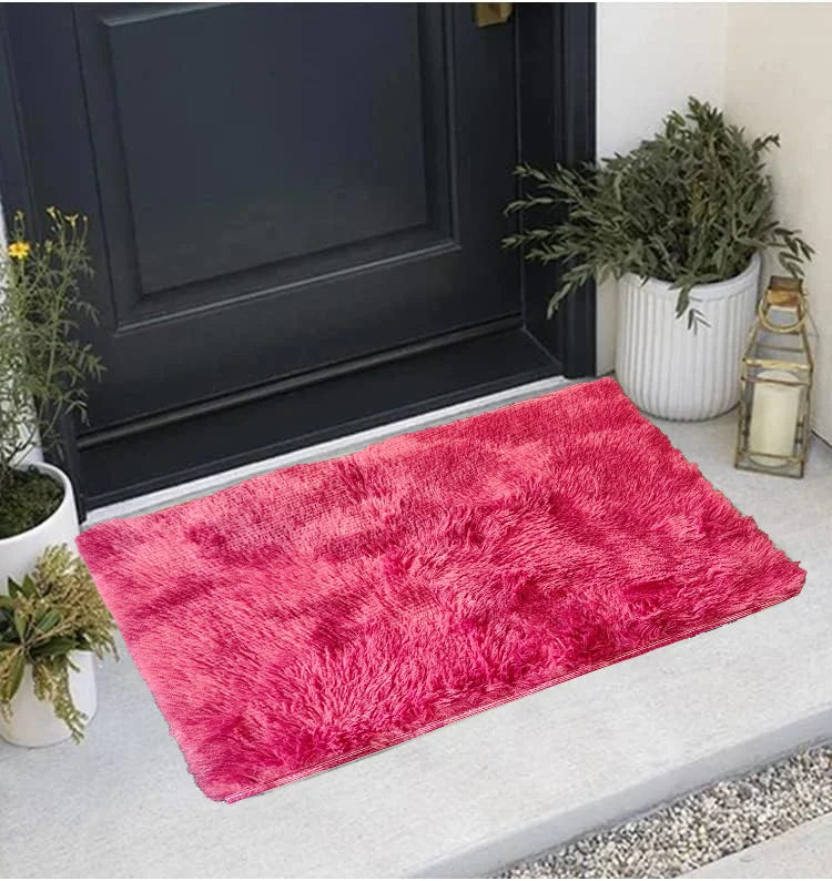 A vibrant pink faux fur area rug placed on a light gray floor next to a dark cabinet and potted greenery.
