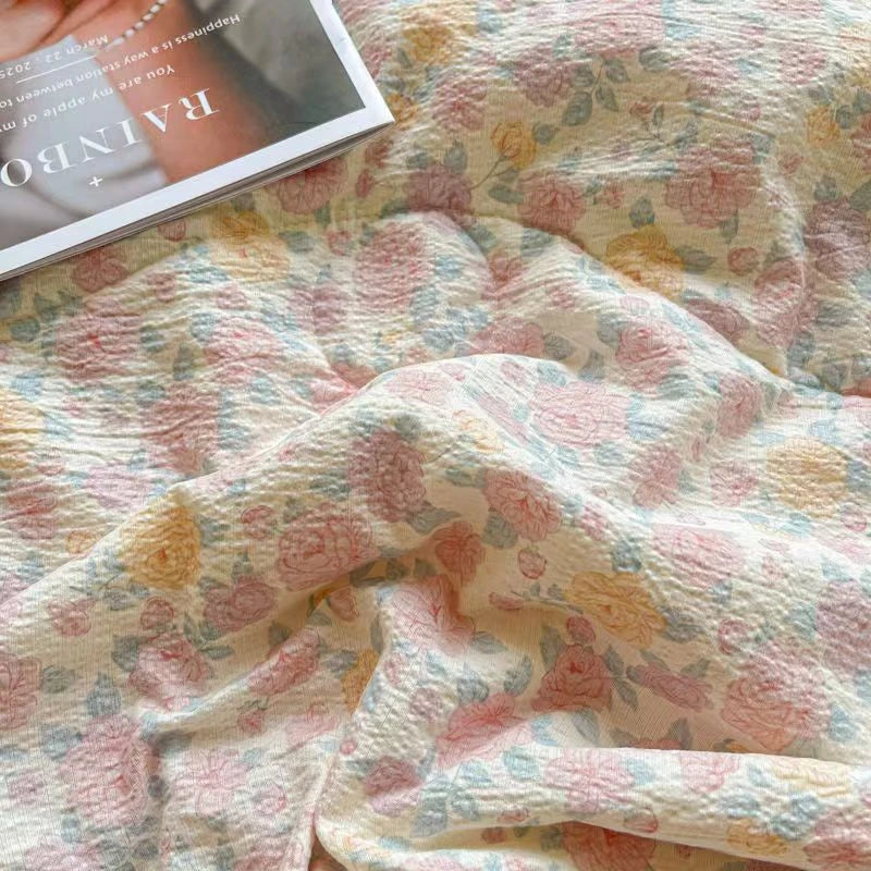 A soft pink and yellow floral print quilt blanket draped on a surface.