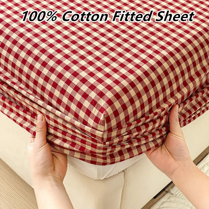 A close-up of a red and cream checkered cotton fitted sheet being held up to show its texture.