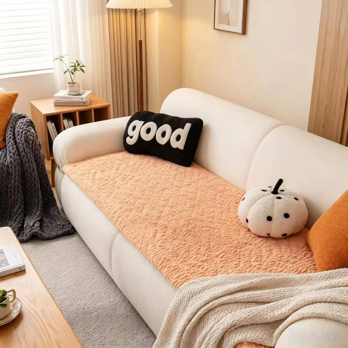A white sofa features an orange flannel pad cover with a black pillow and a white pumpkin decoration.