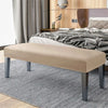 A beige velvet bench slipcover with secure straps placed on a gray striped rug in a bedroom setting.