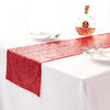 A red sequin table runner is laid on a white tablecloth with silverware and a bottle of liquor in the background.
