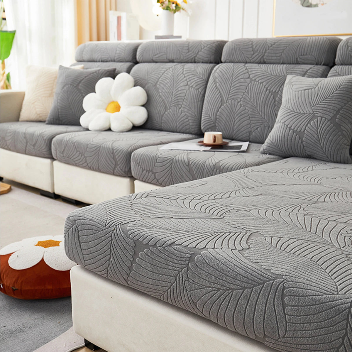 A gray leaf jacquard stretch sofa cover displayed on a modern sectional sofa with white decorative pillows.