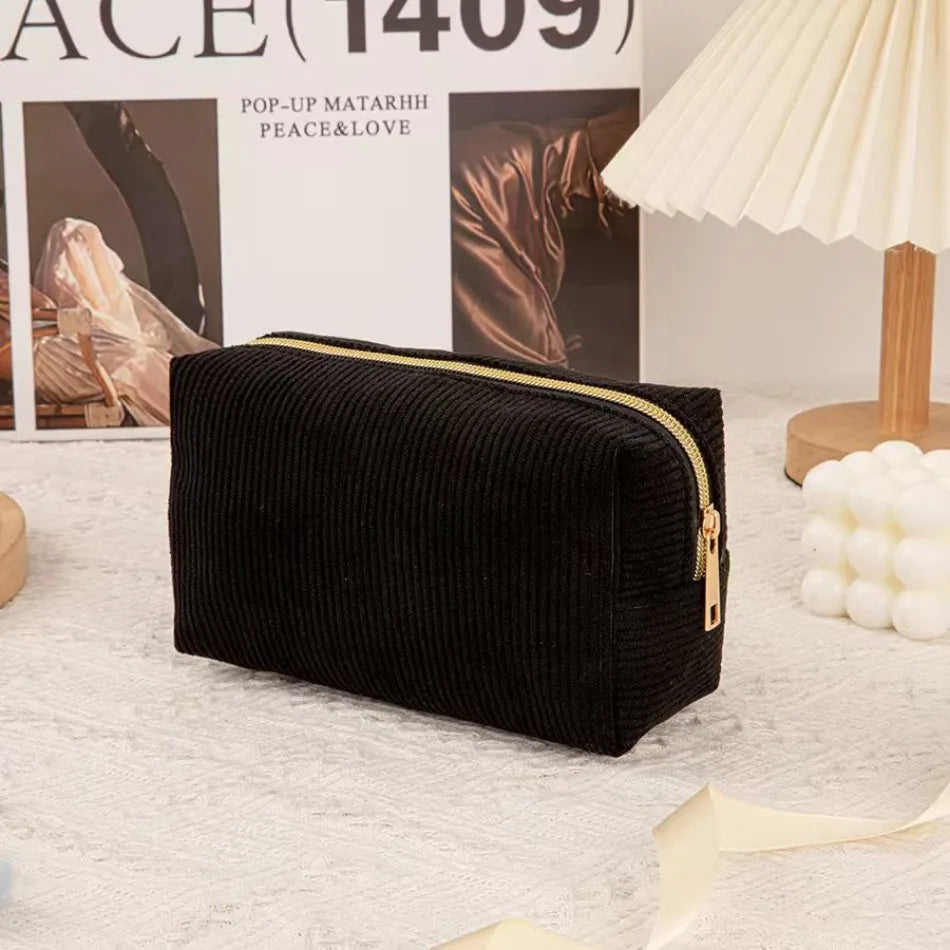 Black textured cosmetic storage pouch with a gold zipper displayed on a white surface.
