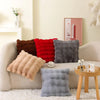 A collection of cozy plush cushion covers in shades of brown, red, and gray resting on a light-colored sofa.