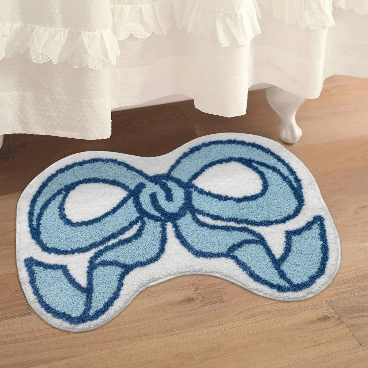 A light blue and white embroidered decorative rug with a bow design placed on a wooden floor.