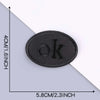 A black embroidered leather patch with the letter OK on it, shown against a gray background.