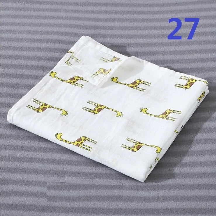 White cotton muslin swaddle blanket with yellow animal print designs folded on a gray background.