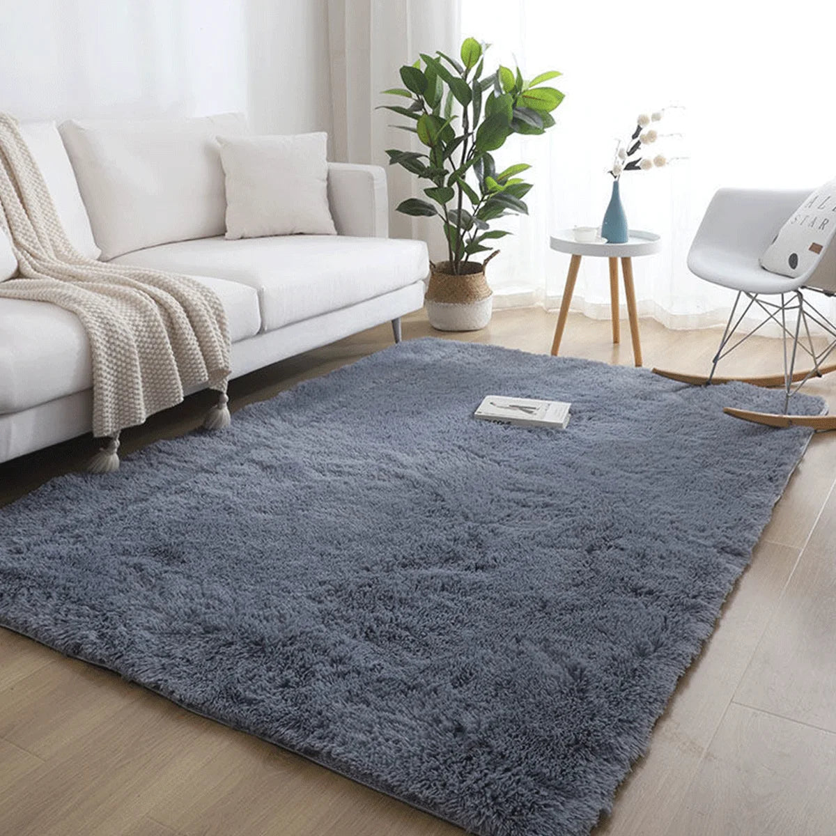 A fluffy gray rug in a modern Nordic style placed on a light wood floor next to a white sofa and potted plant.