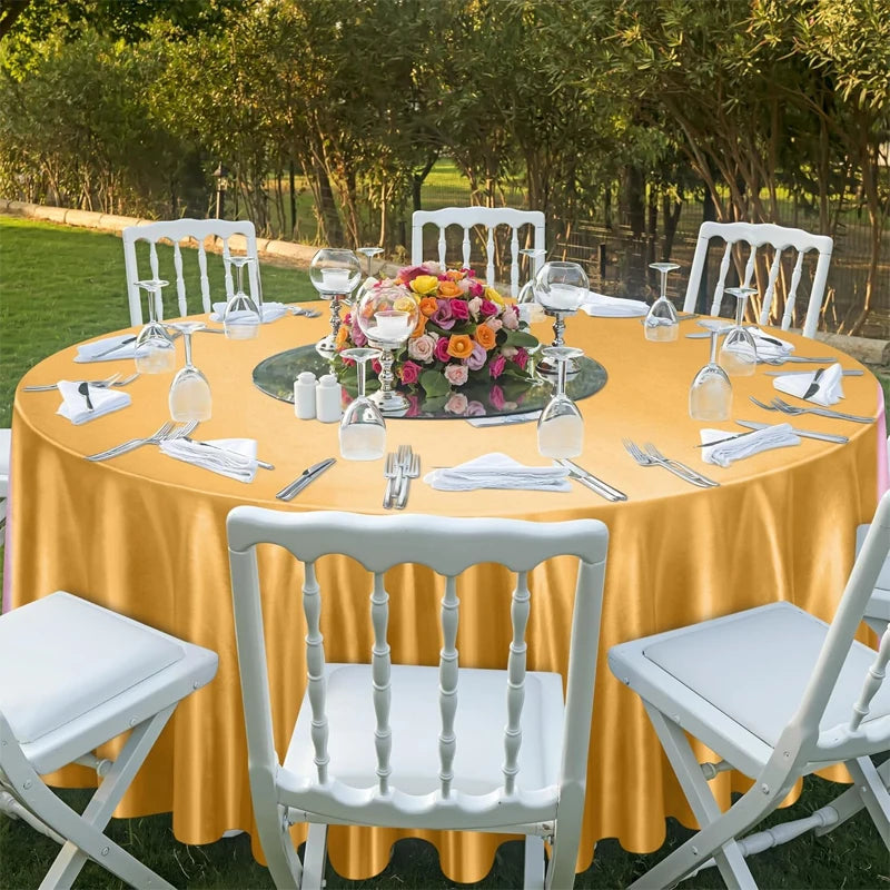 An elegant outdoor dining setup featuring a yellow satin round tablecloth, white chairs, and floral centerpieces.