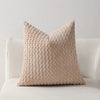 A beige textured decorative pillow cover with a quilted pattern sits on a white sofa.