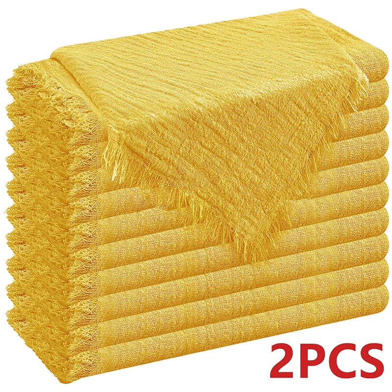 A stack of two golden yellow decorative cloth napkins with fringed edges.