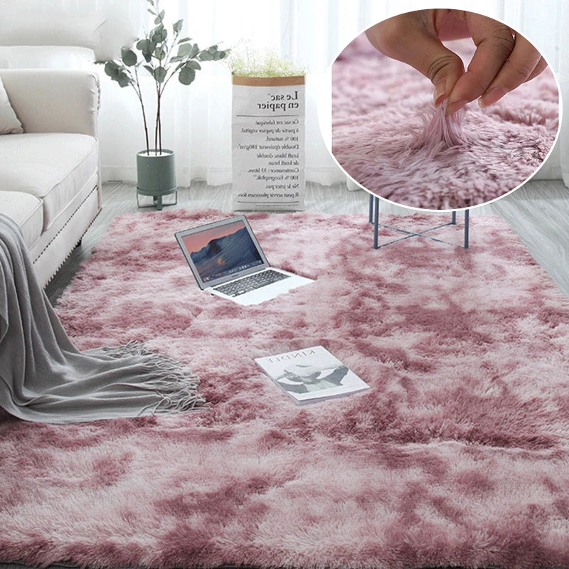 A pink fluffy area rug is displayed on a floor, with a laptop and a plant in the background.