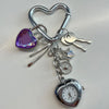 Silver keychain featuring a heart charm, a key, and a pocket watch.