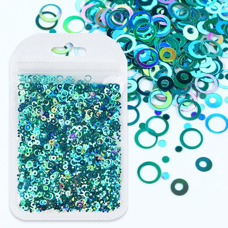 A small white plastic container filled with teal and blue sparkly resin glitter circles and loose glitter pieces.