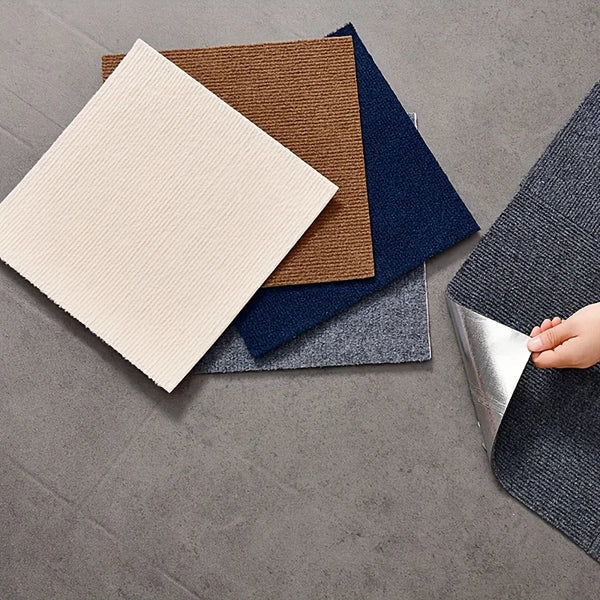 A collection of self-adhesive square carpet tiles in various earthy and dark blue tones are displayed on a gray surface.