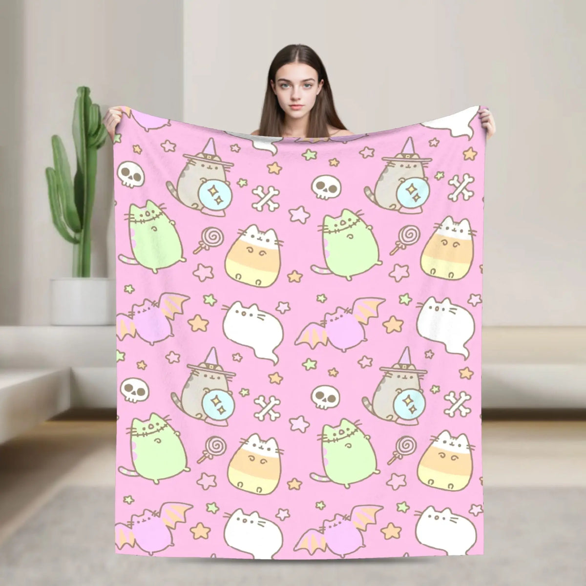 A person is modeling a pink cat plush throw blanket featuring various cute cats and skulls against a light background.