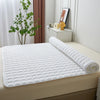 White quilted mattress protector cover placed on a bed, next to a potted plant and decorative items.