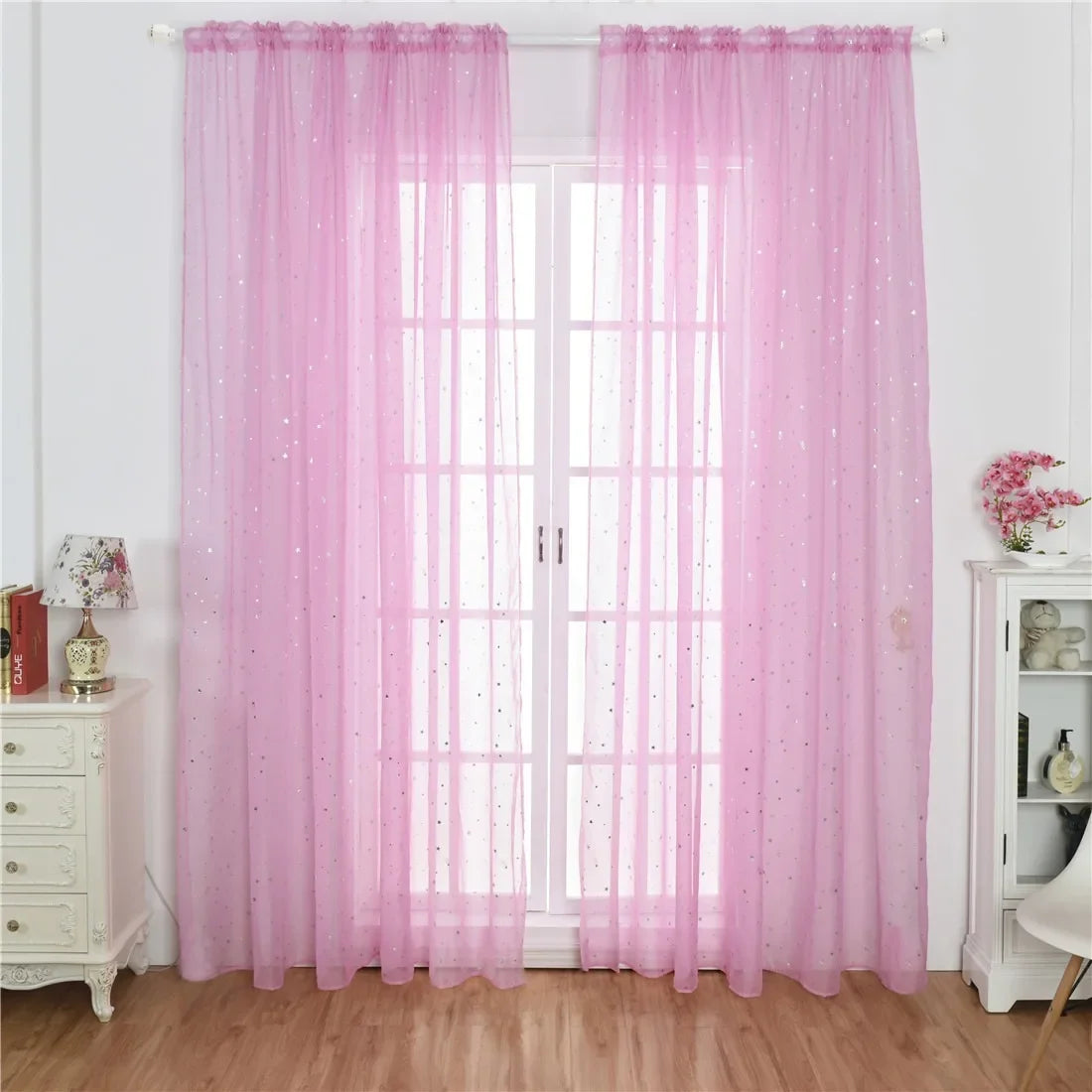 Pink sheer tulle curtains with silver stars hanging over a white glass door.