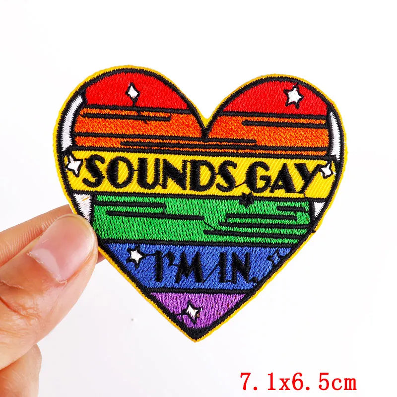 A heart-shaped embroidered patch featuring a rainbow design and the text SOUNDS GAY I'm IN