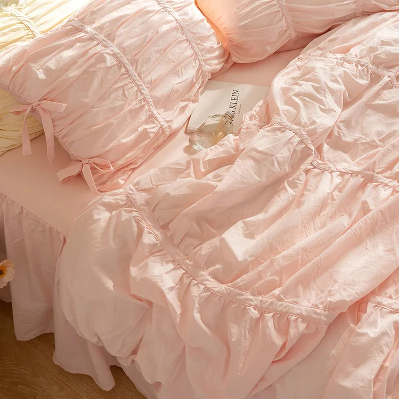 Pink ruffled cotton bedding set with white accents and a small tag on a light pink surface.