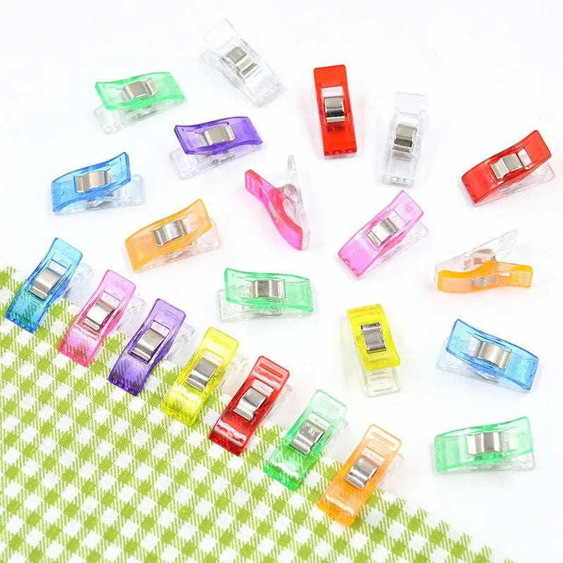 Assorted colorful multipurpose sewing and craft clips arranged on a green checkered surface.