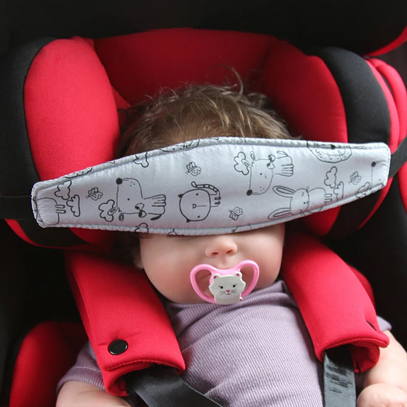 A baby is seated in a red car seat with a gray head support pillow and a pink pacifier.