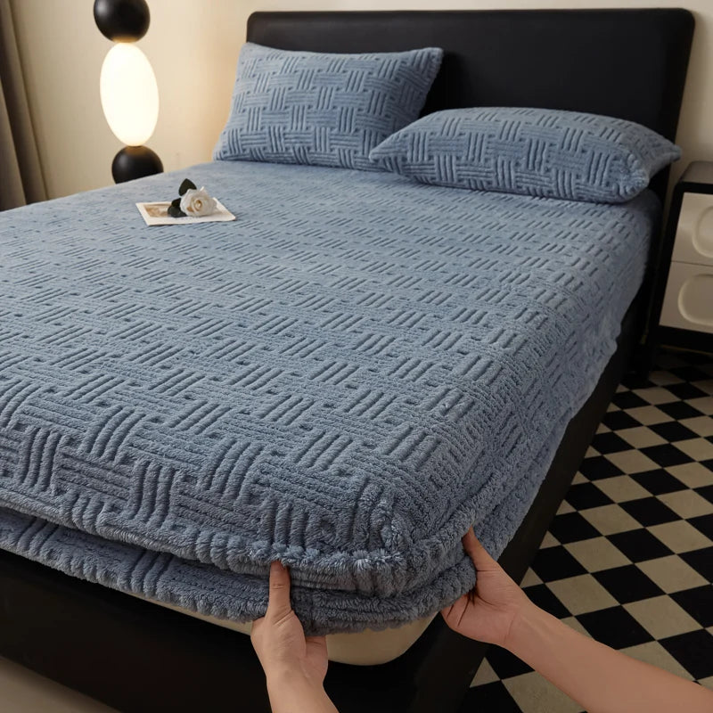 A light blue plush jacquard mattress cover is shown on a bed, with a black headboard and a black and white patterned floor.