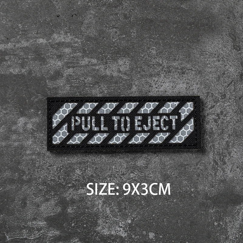 A black hook and loop badge with the text PULL TO EJECT embroidered on it.