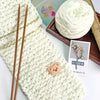 A ball of white chenille knitting yarn next to wooden knitting needles and a small card.
