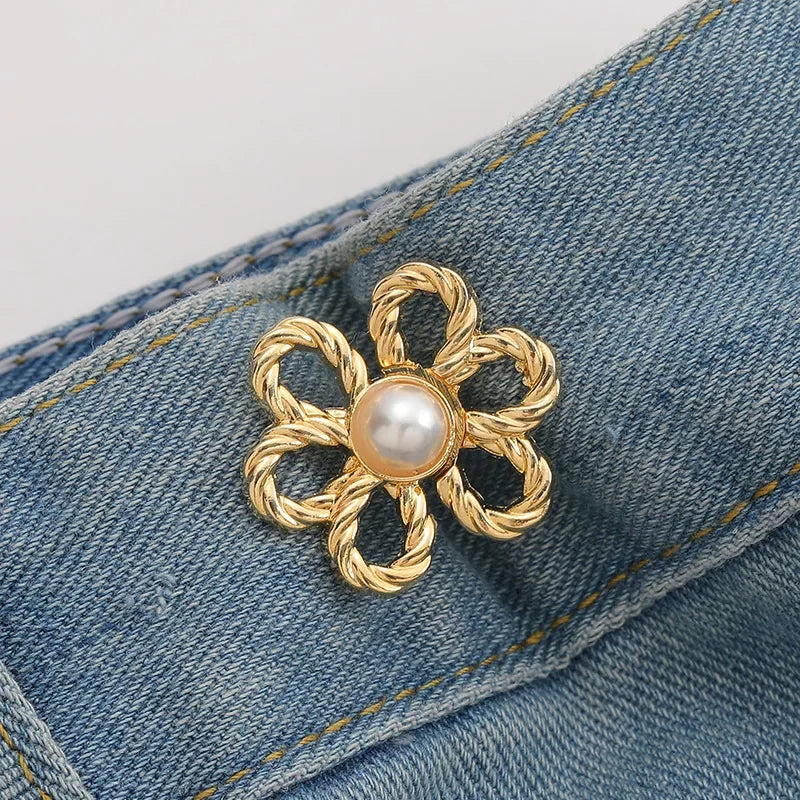 Gold-toned adjustable metal waist clip with a pearl detail attached to a denim fabric.