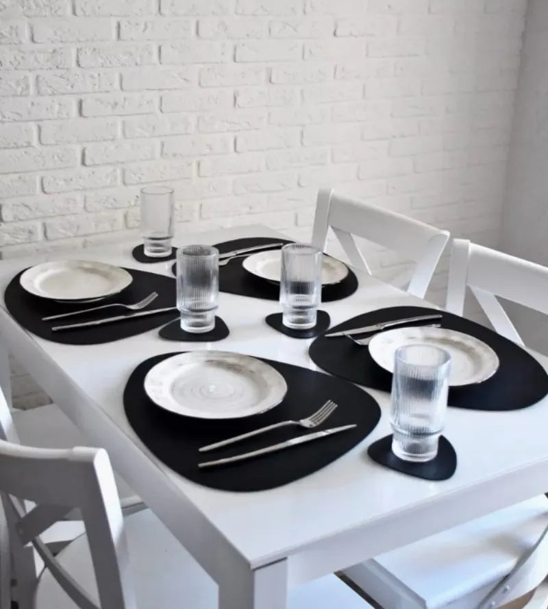 A white dining table set with black placemats, silverware, and clear glasses.