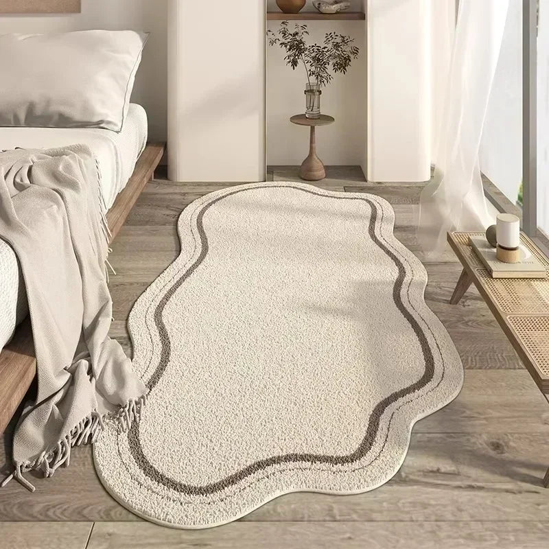 A cream colored irregular plush area rug with subtle gray edging placed on a light wood floor.