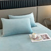 Light blue luxury velvet bedding set with pillows and a small tray of cream candles on a bed.