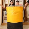 A bright yellow heavy duty waterproof storage bag is displayed in front of a wooden shelf with clothing.