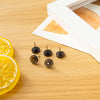 A collection of transparent round head push pins is displayed on a wooden surface next to a slice of lemon.