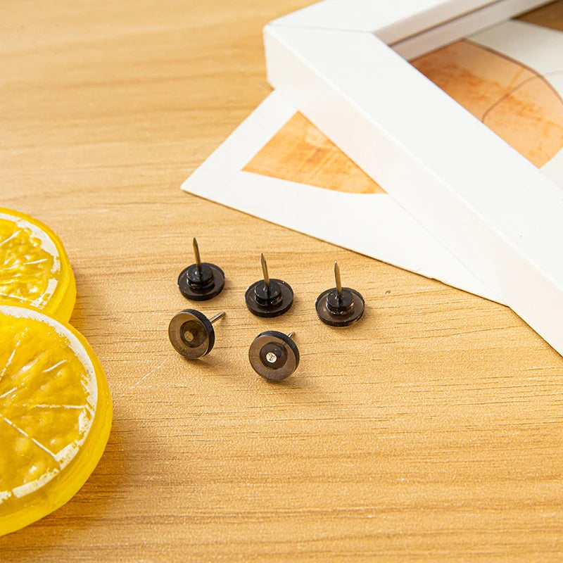 A collection of transparent round head push pins is displayed on a wooden surface next to a slice of lemon.