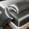 A close-up of a smooth gray satin fitted sheet draped over a mattress.