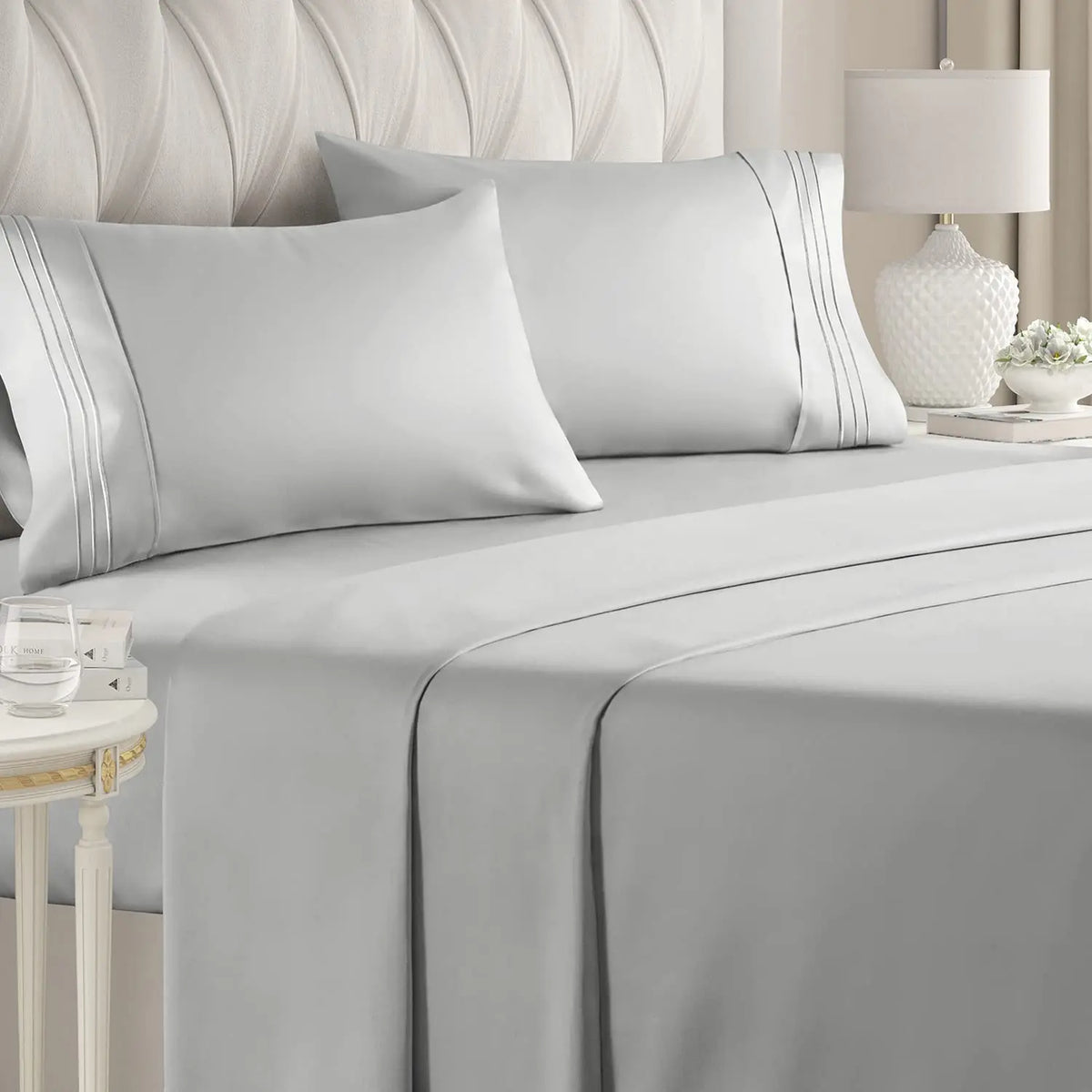 A set of four white luxury microfiber bed sheets with piping and deep pockets on a bed.